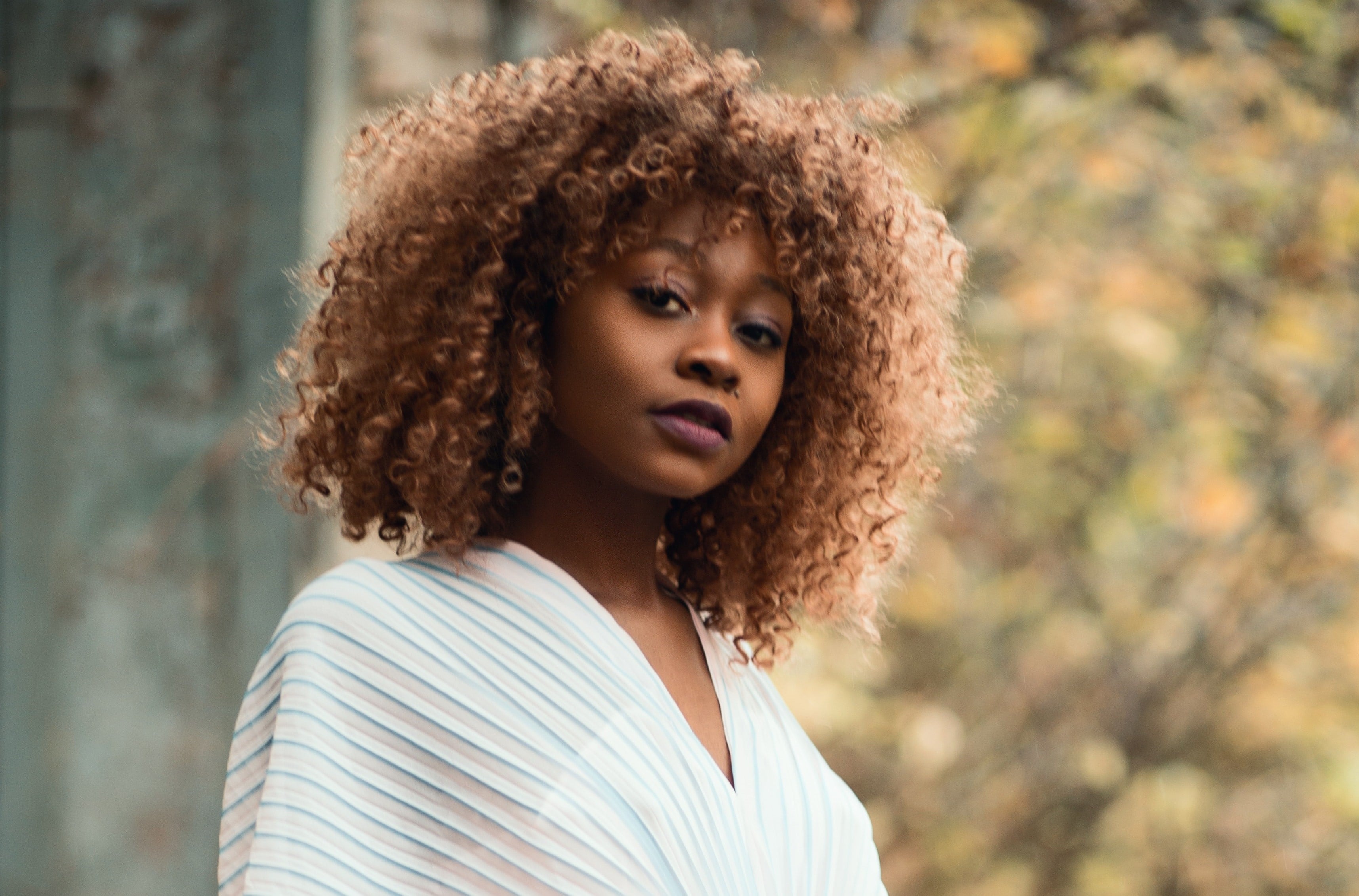  Mulher negra com cabelo encaracolado e blusa listrada, ao ar livre com fundo desfocado