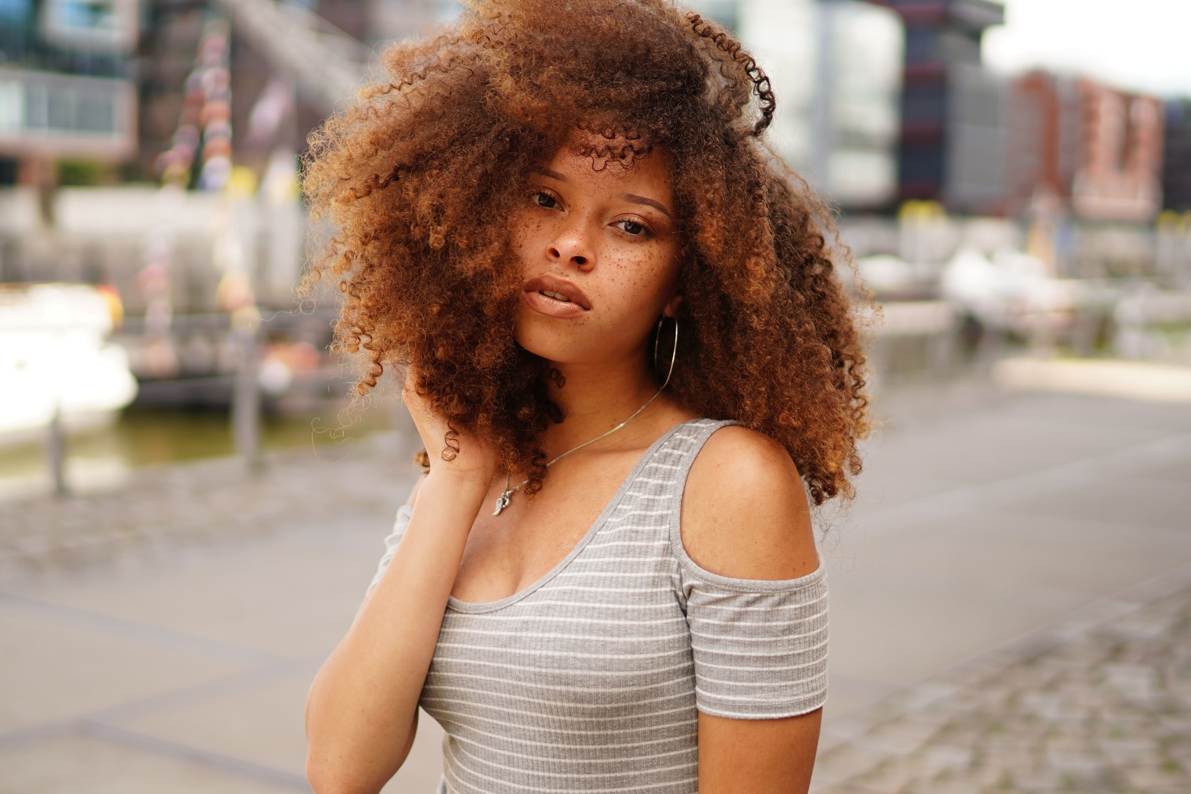  Mulher com cabelo cacheado e top cinza listrado em cenário urbano