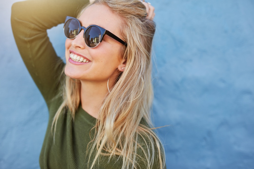  Mulher sorridente com óculos de sol e blusa verde em fundo azul