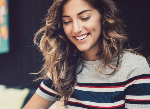  ﻿Mulher branca sorridente com cabelos ondulados e blusa listrada