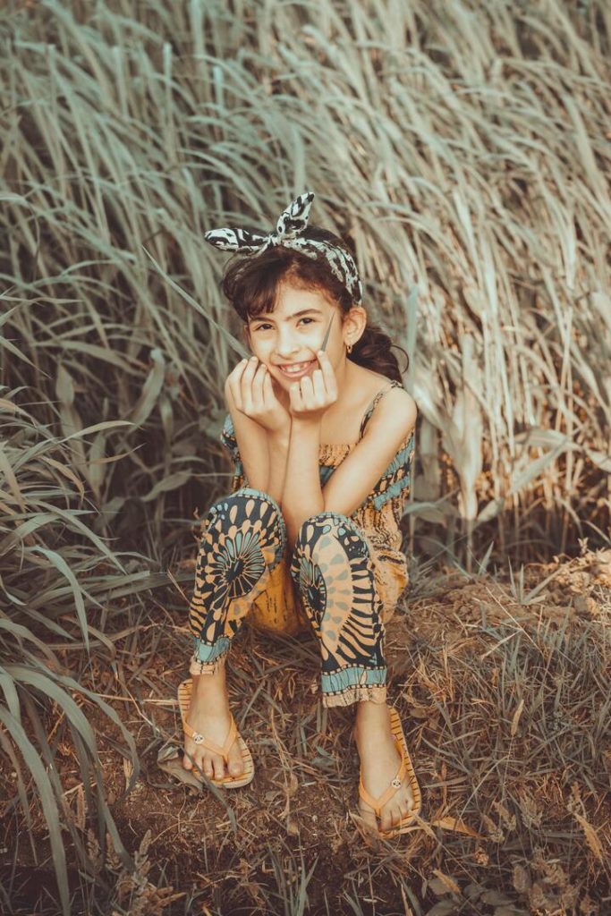 menina sentada no chão com o cabelo amarrado e sorrindo