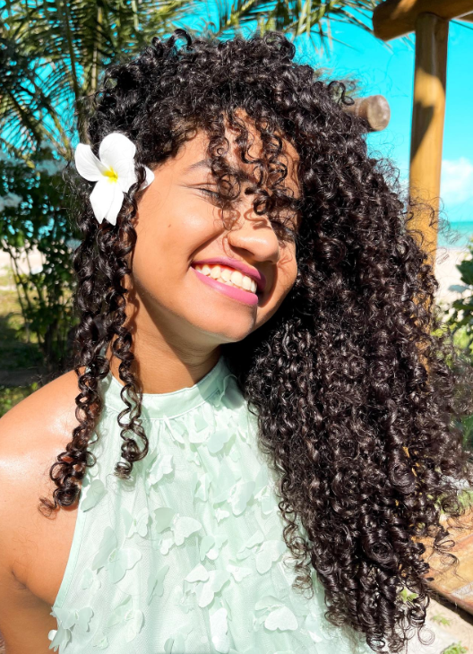  mulher negra sorrindo com flor branca no cabelo cacheado