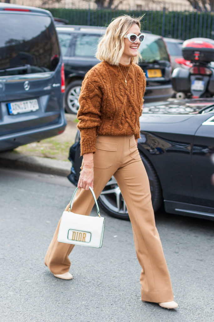 mulher branca usando blusa de lã marrom e bolsa branca