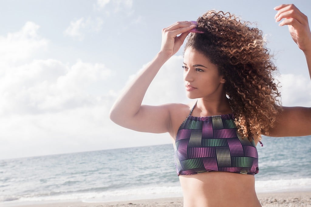  Mulher jovem, na praia, passando o pente garfo no cabelo cacheado