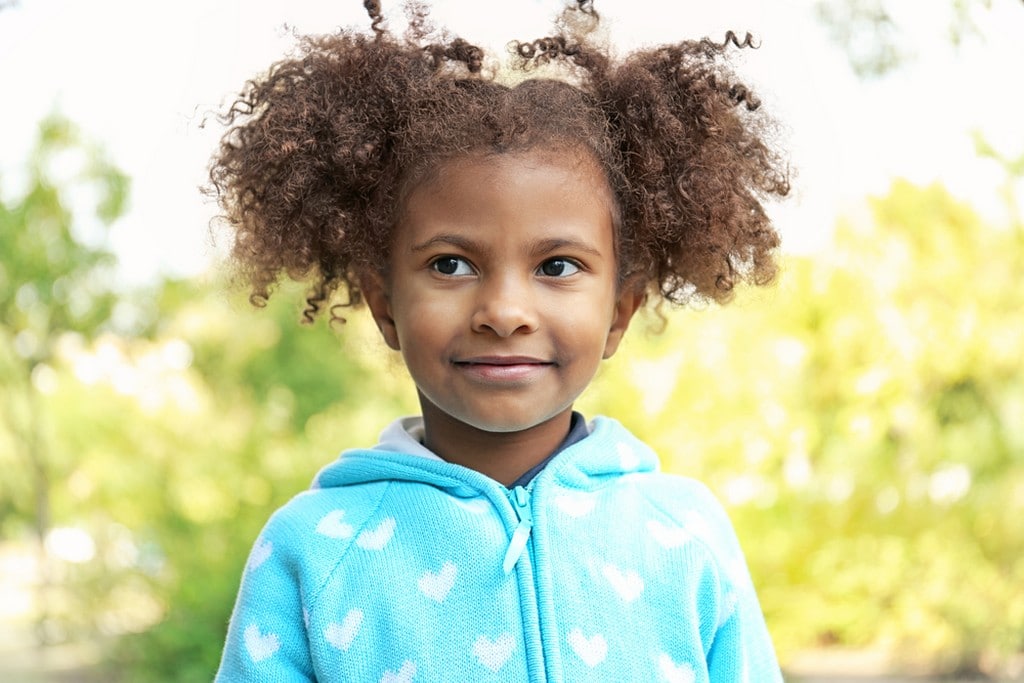  Criança de cabelo cacheado, com penteado de Maria-chiquinha