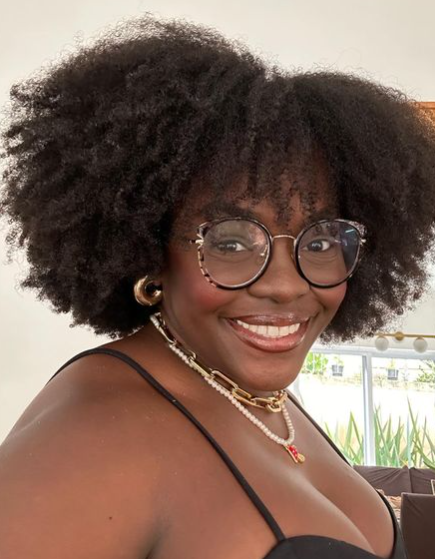  Mulher negra de cabelo black power usando óculos e sorrindo para a foto