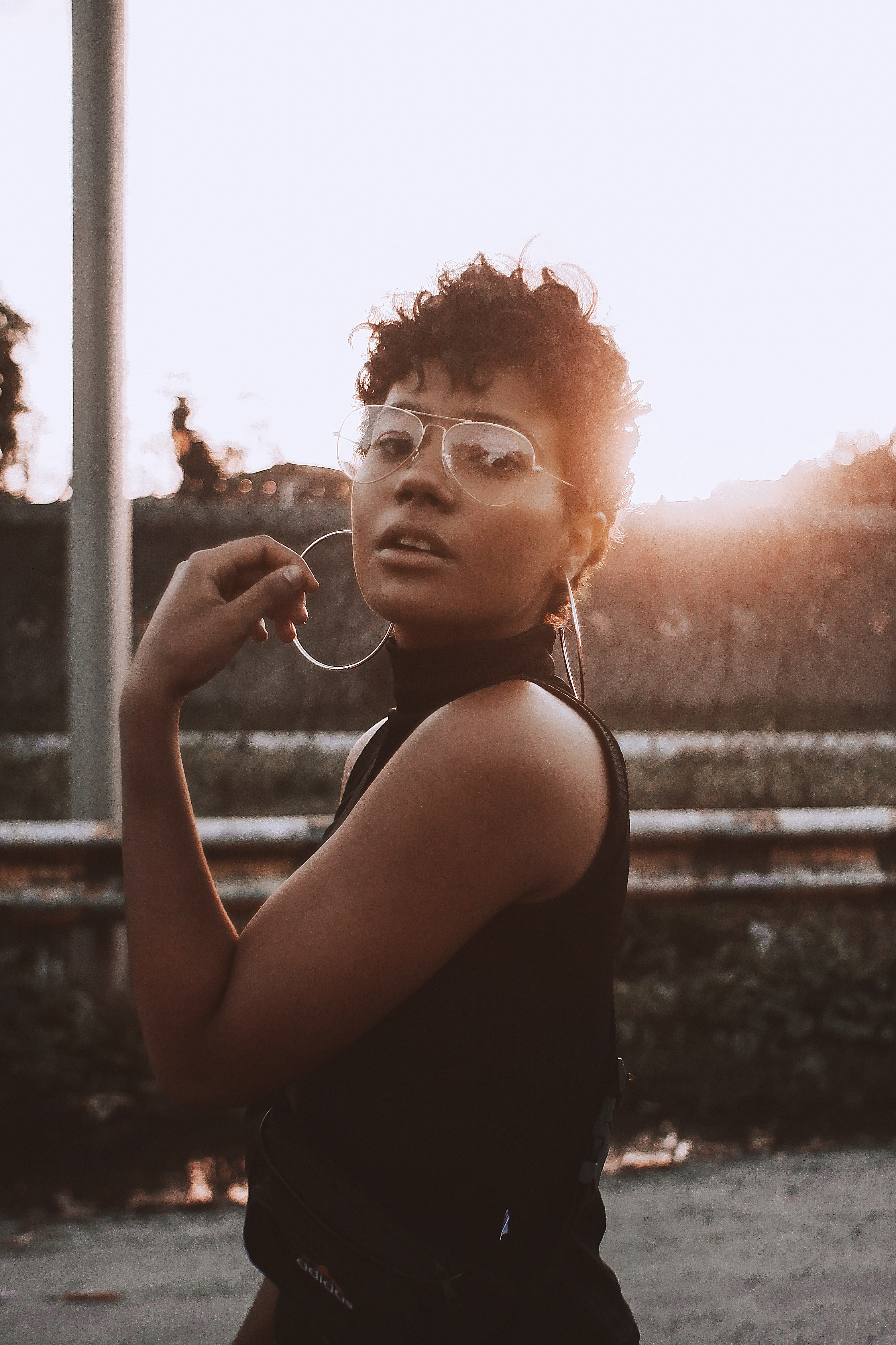  Mulher negra com cabelo cacheado e óculos, posando ao pôr do sol