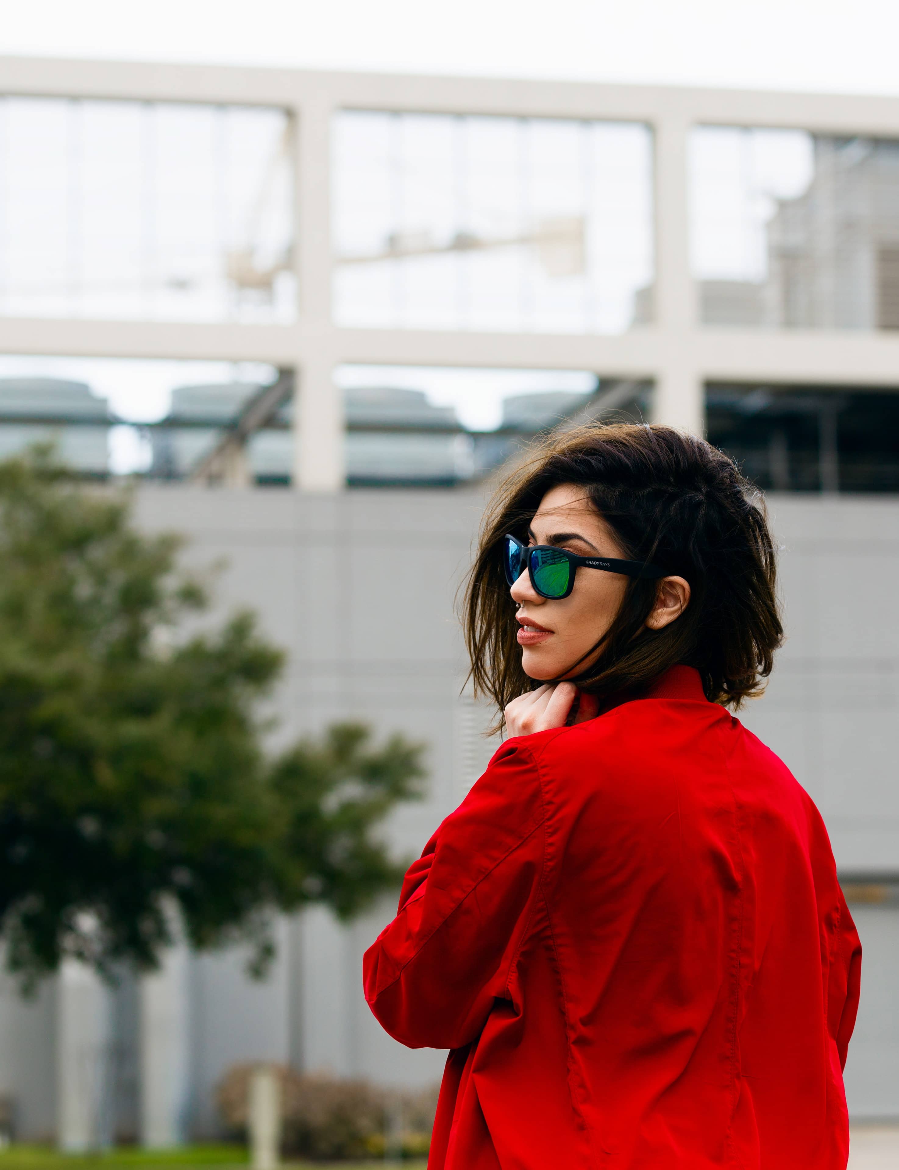  Mulher elegante com camisa vermelha e óculos de sol, vista de perfil em ambiente urbano