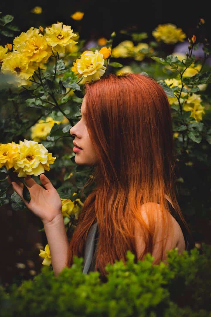  Mulher branca, de cabelo liso, ruivo e longo (alisados naturalmente), segurando uma flor amarela