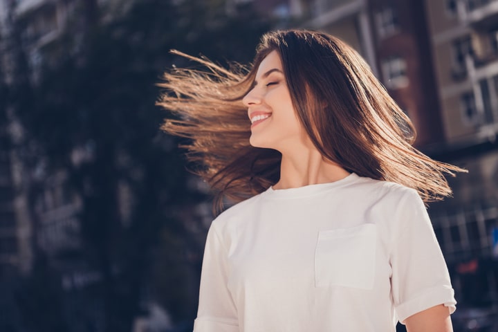  Mulher de cabelo lisos ao vento, castanho, um pouco abaixo do ombro, fios alinhados e hidratados (características do realinhamento capilar)