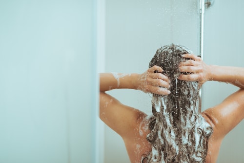  Mulher debaixo do chuveiro, lavando o cabelo com shampoo de limpeza profunda