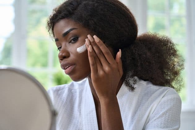 Mulher de pele negra passando creme no rosto