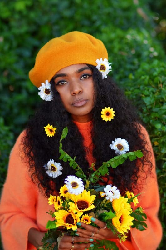 Moça com boina amarela e roupa com laranja, um estilo anos 2000.