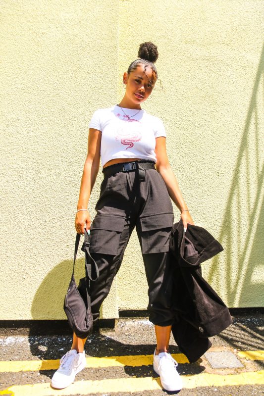Moça com a calça cargo da cor preta e uma blusa branca.