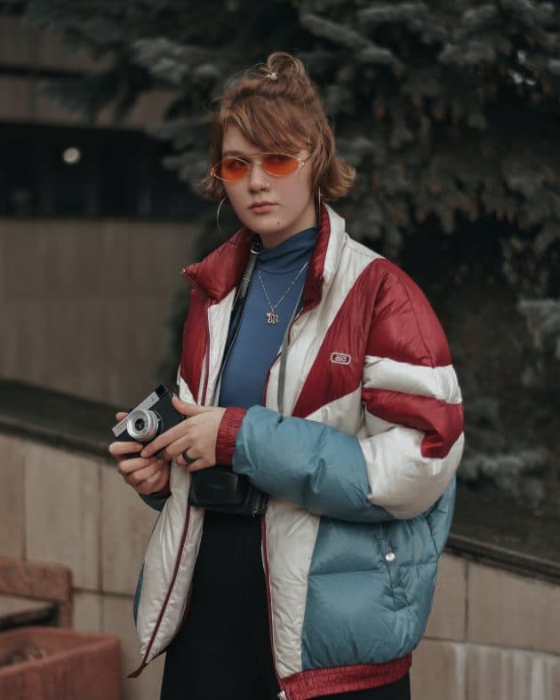 Uma moça com óculos coloridos que tem só a lente vermelha, um estilo anos 2000.
