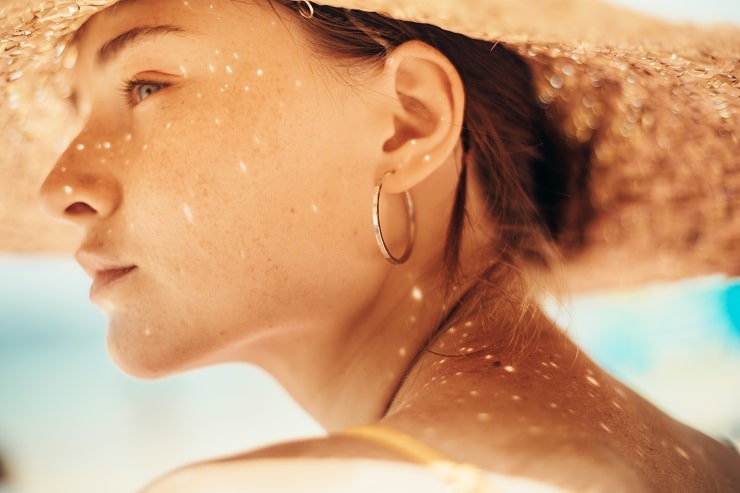  Mulher branca tomando sol na praia, com um chapéu para proteção contra os raios uv