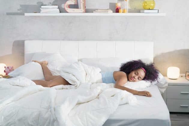 Mulher de cabelo cacheado castanho escuro, com mechas roxas, dormindo na cama