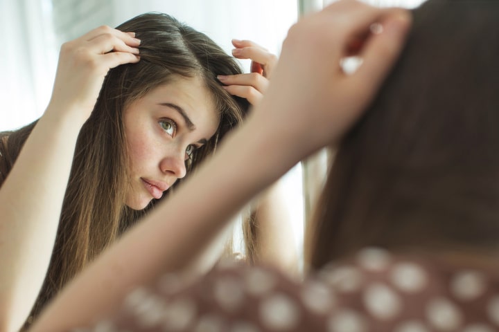  Mulher de cabelo liso longo e loiro escuro, dividindo-o perto da raiz, com as mãos, para observar o couro cabeludo