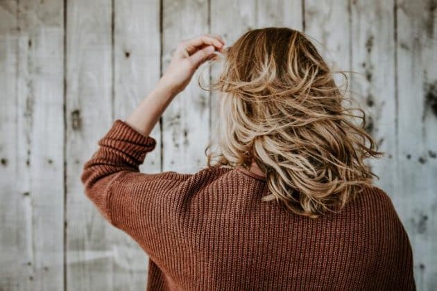 Mulher de costas, com o cabelo ondulado loiro, com mechas, corte acima do ombro, em movimento