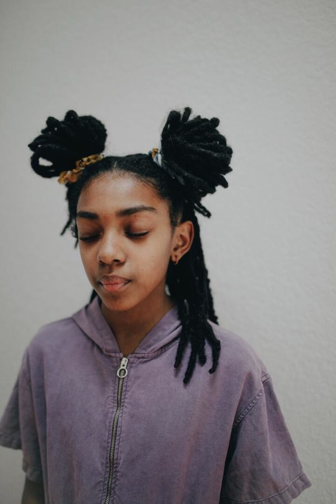 Mulher jovem, com dreads no cabelo e penteado com coque duplo e parte dos dreads soltos