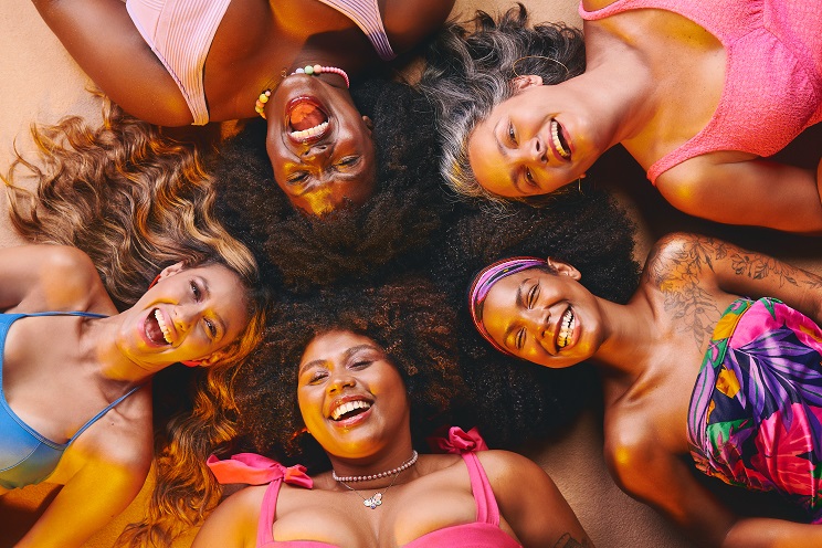  Imagem da campanha de verão Salon Line: 5 mulheres com diferentes corpos, tom de pele e cabelo, deitadas na areia da praia, com as cabeças juntas (formando um círculo)