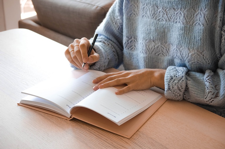  Mulher fazendo anotações das suas tarefas diárias em um caderno. Ótima sugestão de como se organizar no dia a dia