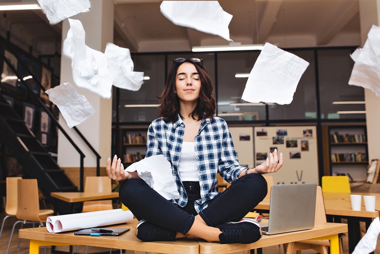  Mulher no trabalho em posição de meditação, enquanto papéis e documentos voam ao redor dela