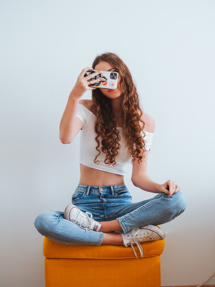 Mulher com blusa curta branca, decote ciganinha, calça jeans clara e tênis branco