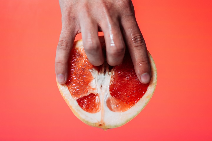  Mãos femininas tocando uma laranja, representando o prazer feminino.