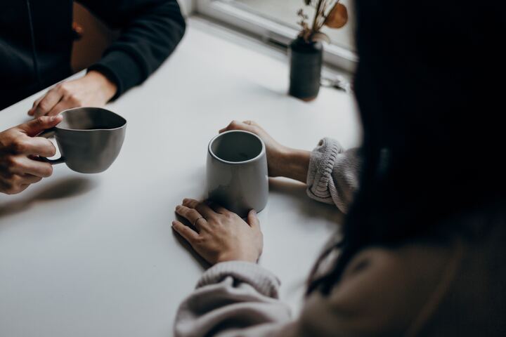 mulher com as mãos sobre a mesa, segurando uma caneca de café