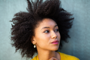 Mulher com cabelo afro volumoso e rosto suave, usando uma blusa amarela. A imagem destaca a beleza e a naturalidade do cabelo cacheado, ideal para temas de autoestima e cuidados capilares.